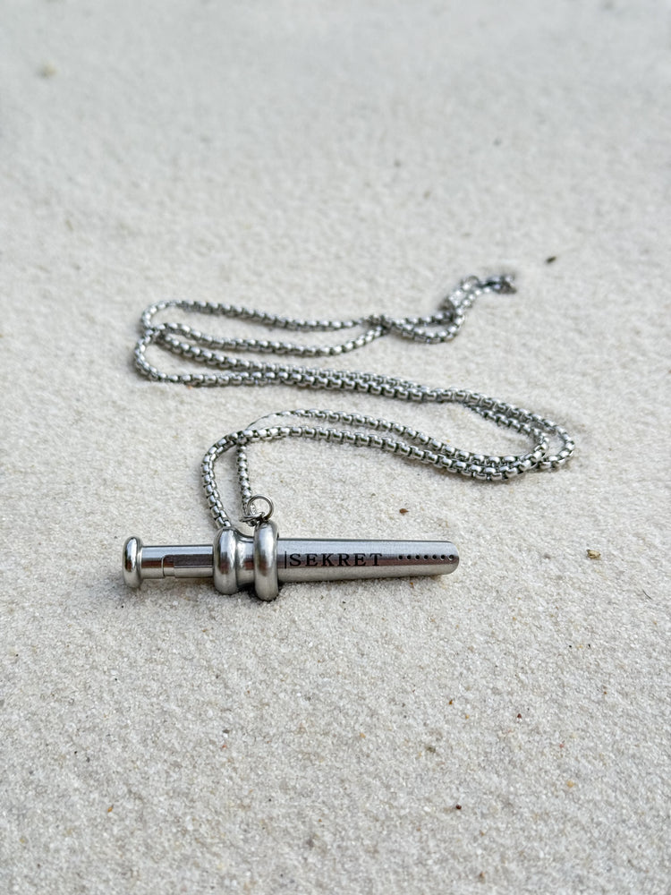 Sekret pendant on a stainless steel box chain, resting on white sand